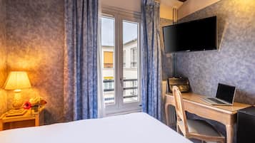 Ein Hotelzimmer mit Bett, Schreibtisch mit Laptop, Fernseher an der Wand und einem Fenster mit Vorhängen.