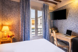 A hotel room with a bed, a desk with a laptop, a TV on the wall, and a window with curtains.