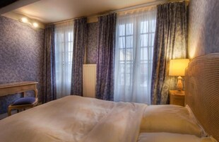 Une chambre d’hôtel avec un grand lit, une table de chevet en bois avec une lampe, une chaise et une fenêtre avec des rideaux.