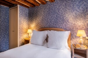 A neatly made bed with white linens, a wooden headboard, and two bedside lamps.