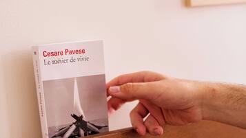 A hand holding a book titled "Le métier de vivre" by Cesare Pavese.