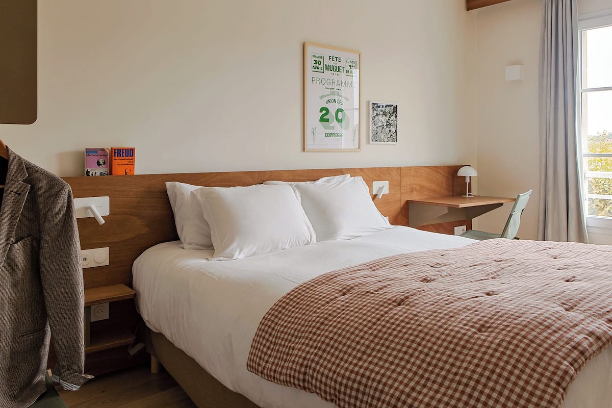 Habitación de hotel con una cama grande, cabecera de madera, escritorio con silla y ventana con cortinas.