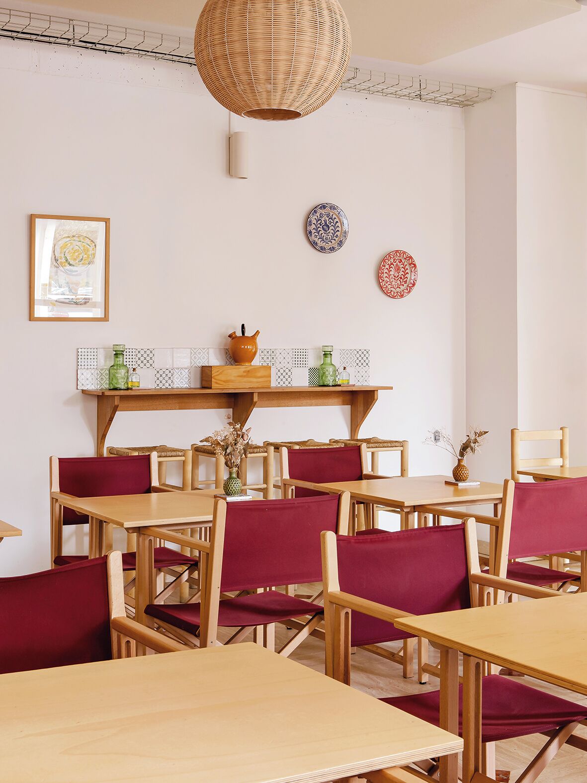 A dining area with wooden tables and chairs, a hanging light fixture, and decorative plates on the wall.
