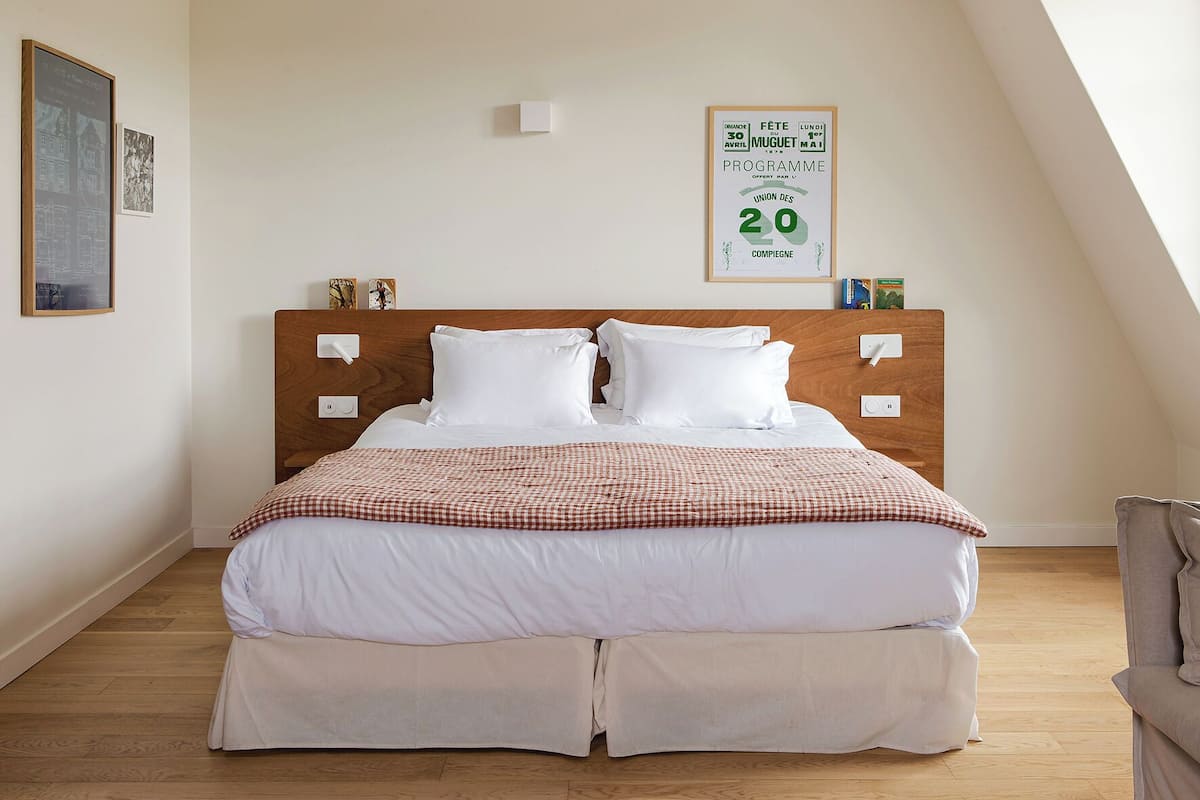Una cama bien hecha con una manta a cuadros, un cabecero de madera y un cartel enmarcado en la pared.