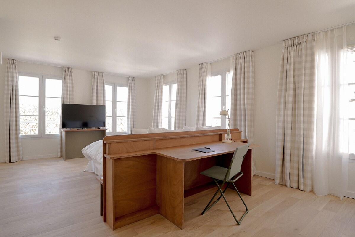 A bedroom with a wooden desk, a chair, a bed, and a TV.