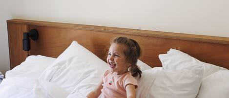 Un niño sentado en una cama con ropa blanca y un cabecero de madera.