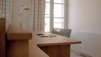A wooden desk with a laptop and glasses, a lamp, and a chair in a room with a window and curtains.