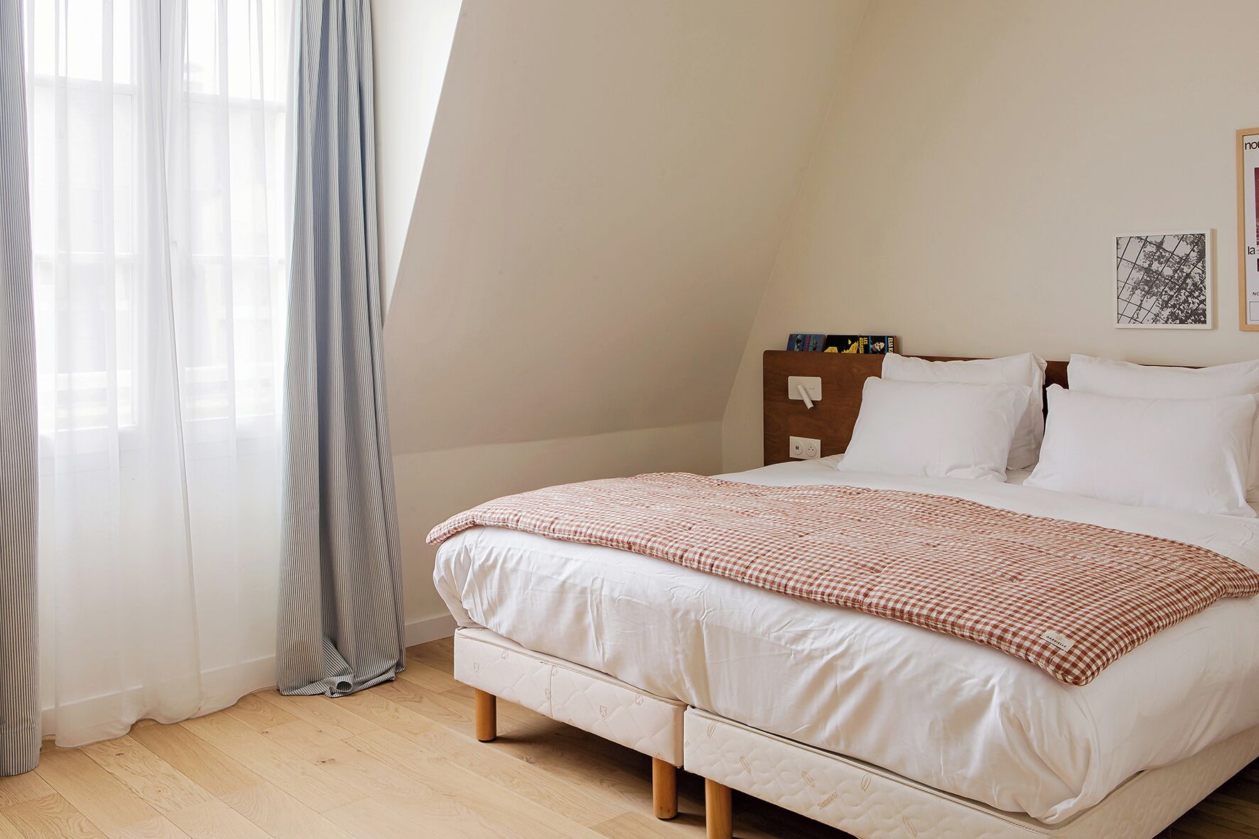 A bedroom with a bed, a bedside table, a window with curtains, and a wall-mounted picture.