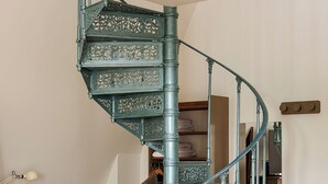 Een wenteltrap met gedecoreerde metalen balustrades in een ruimte met houten vloeren, een bureau en een stoel.