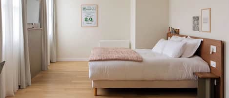 Une chambre à coucher avec un lit, une table de chevet, une commode, un miroir et une affiche accrochée au mur.