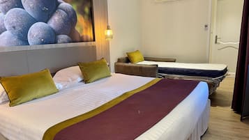A hotel room with a large bed, two smaller beds, a headboard, a wall-mounted air conditioner, and a door.