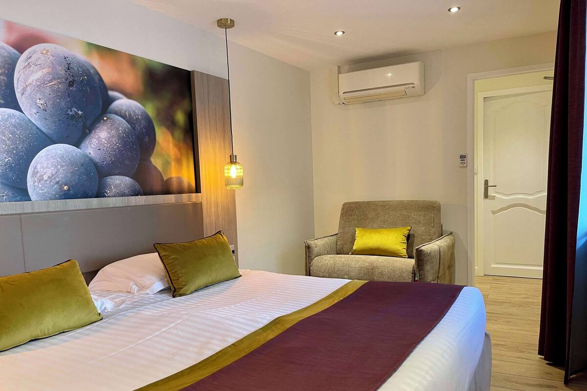 Une chambre d’hôtel avec un grand lit, une chaise, un appareil de climatisation et un tableau au mur.
