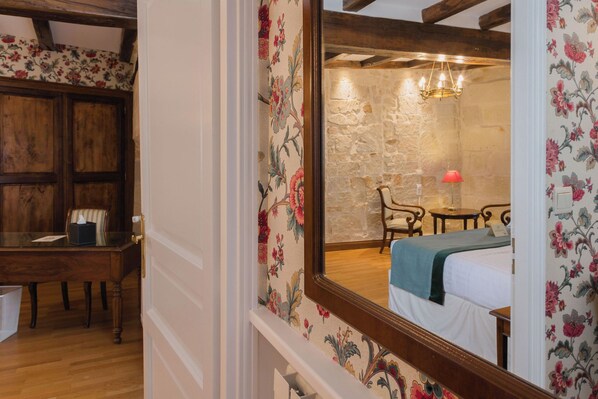 A bedroom with a stone wall, a bed with a green blanket, a wooden desk, and a chair. - Best Western Hotel De France (Chinon)