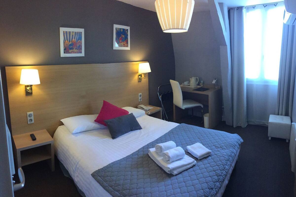 Une chambre d’hôtel avec un lit, des lampes de chevet, un bureau, une chaise et une fenêtre avec des rideaux.