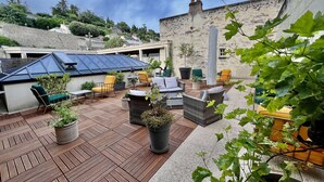 A rooftop patio with outdoor seating, potted plants, and a stone building in the background.