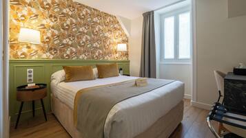 A hotel room with a large bed, two bedside lamps, a small table, and a window with curtains.