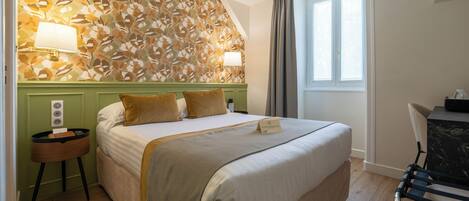 A hotel room with a large bed, two bedside lamps, a small table, and a window with curtains.