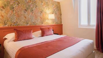 Une chambre d’hôtel avec un grand lit, un papier peint à motifs floraux, une table de chevet et une fenêtre avec des rideaux.