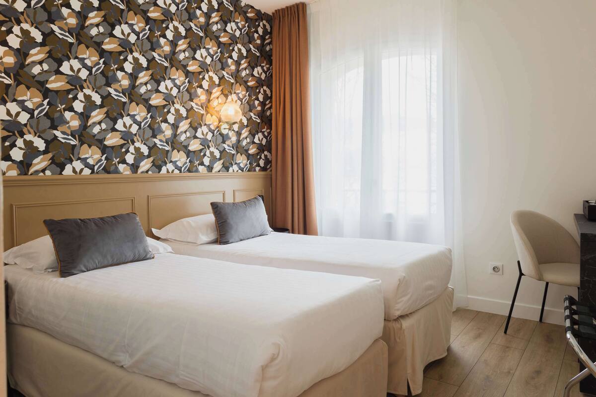 Une chambre d’hôtel avec deux lits, un bureau, une chaise et un mur décoré d’un motif de feuilles.