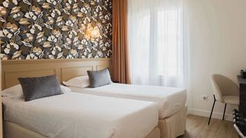 A hotel room with two beds, a desk, a chair, and a decorative leaf-patterned wall.
