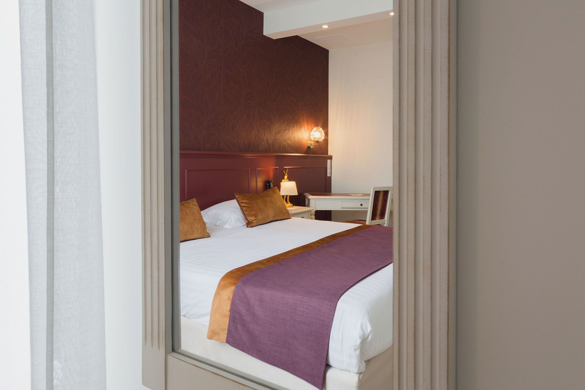 A hotel room with a bed, a nightstand, a lamp, and a wall-mounted light.