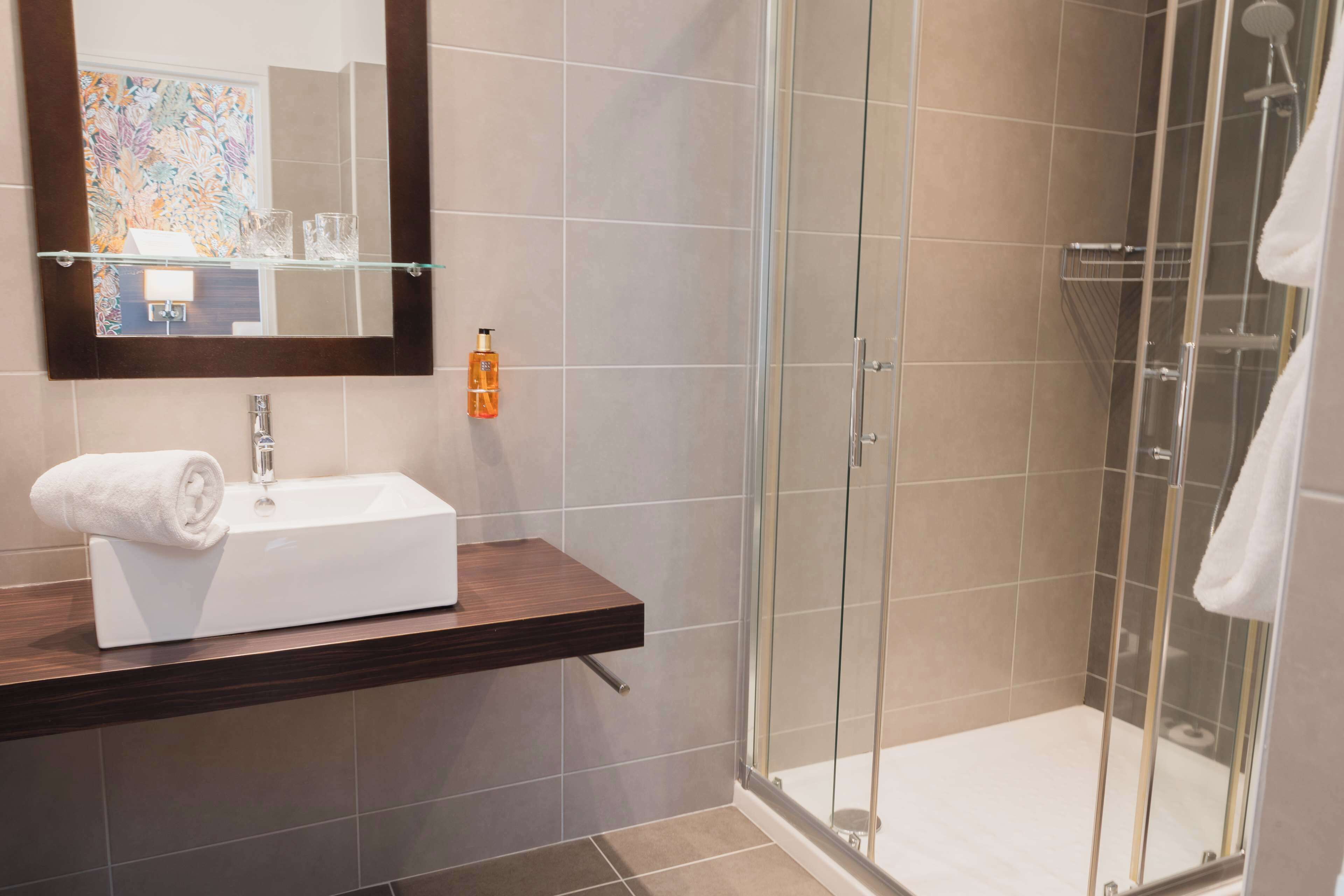 A modern bathroom with a glass shower enclosure, a white sink, and a wooden vanity.