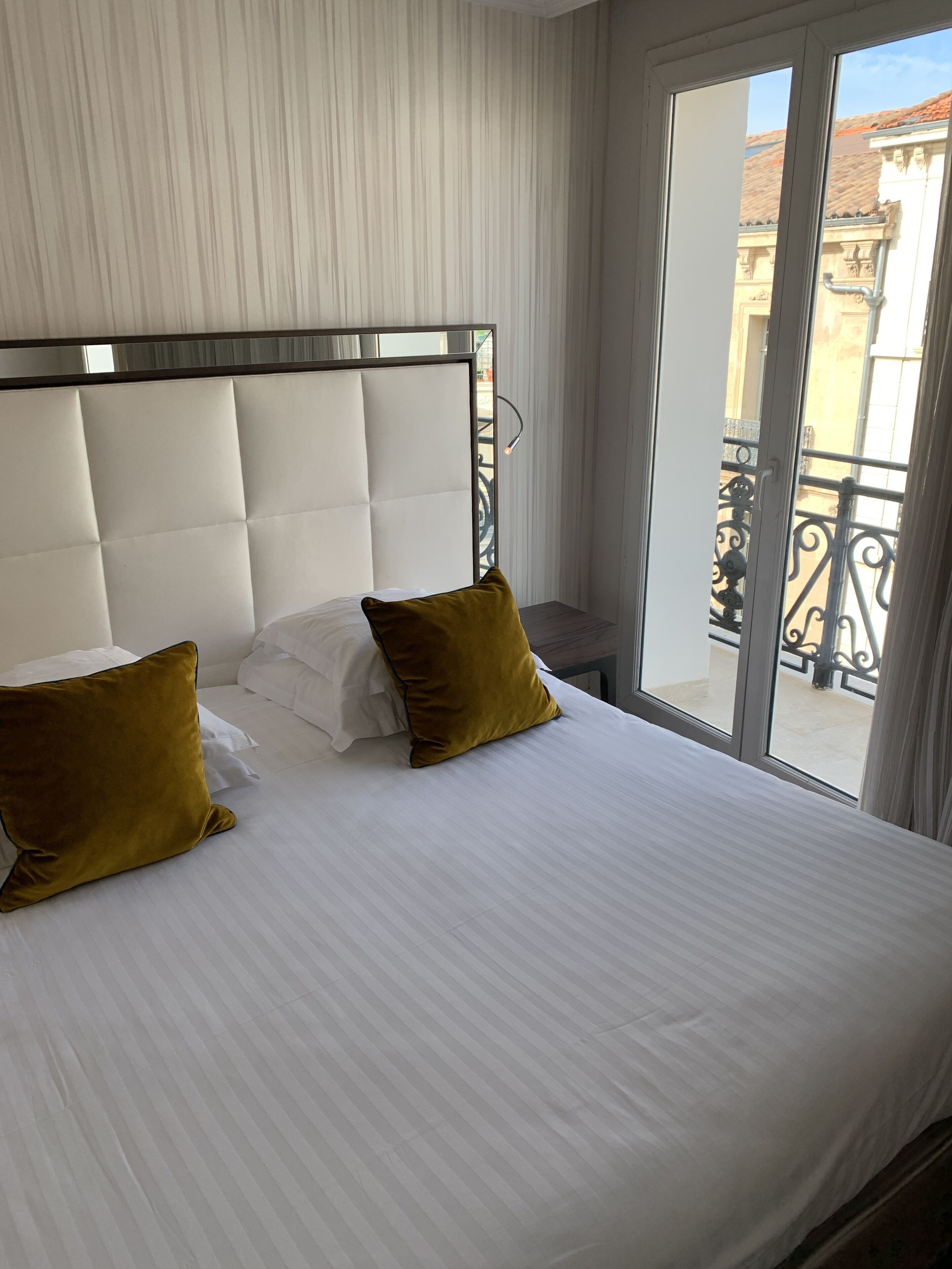 Une chambre d’hôtel avec un grand lit, du linge de lit blanc et deux oreillers de couleur jaune moutarde.