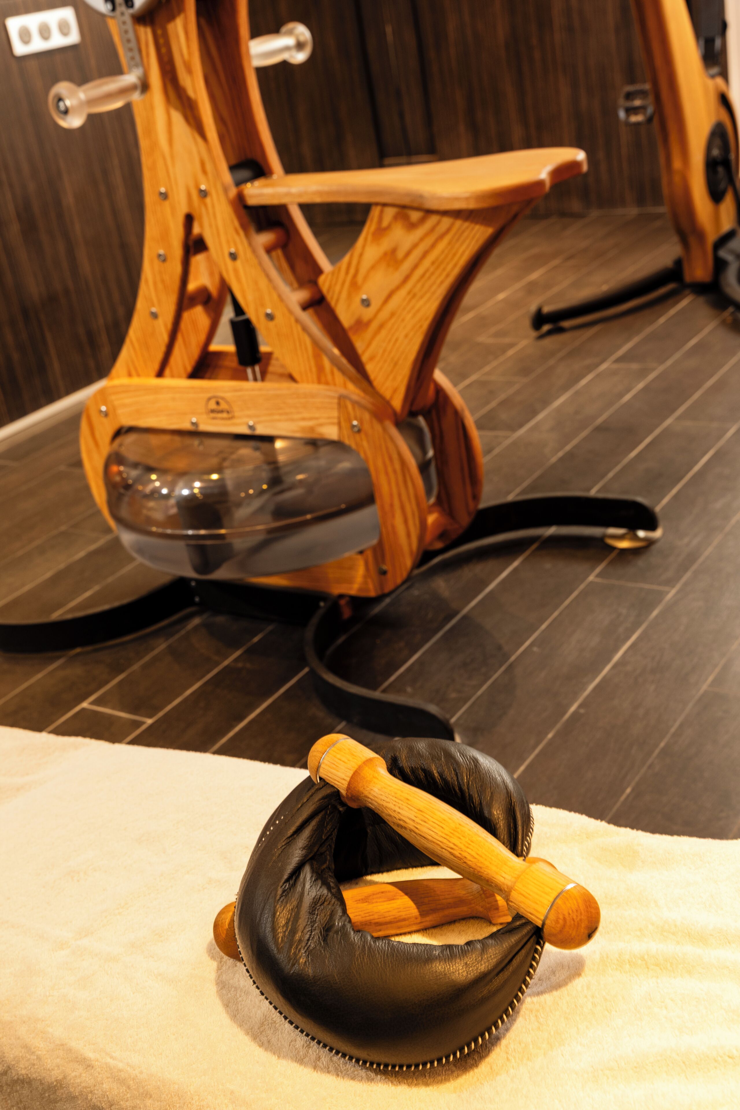 Een massagestoel met houten frame en een zwarte lederen zitting, staand op een betegelde vloer.
