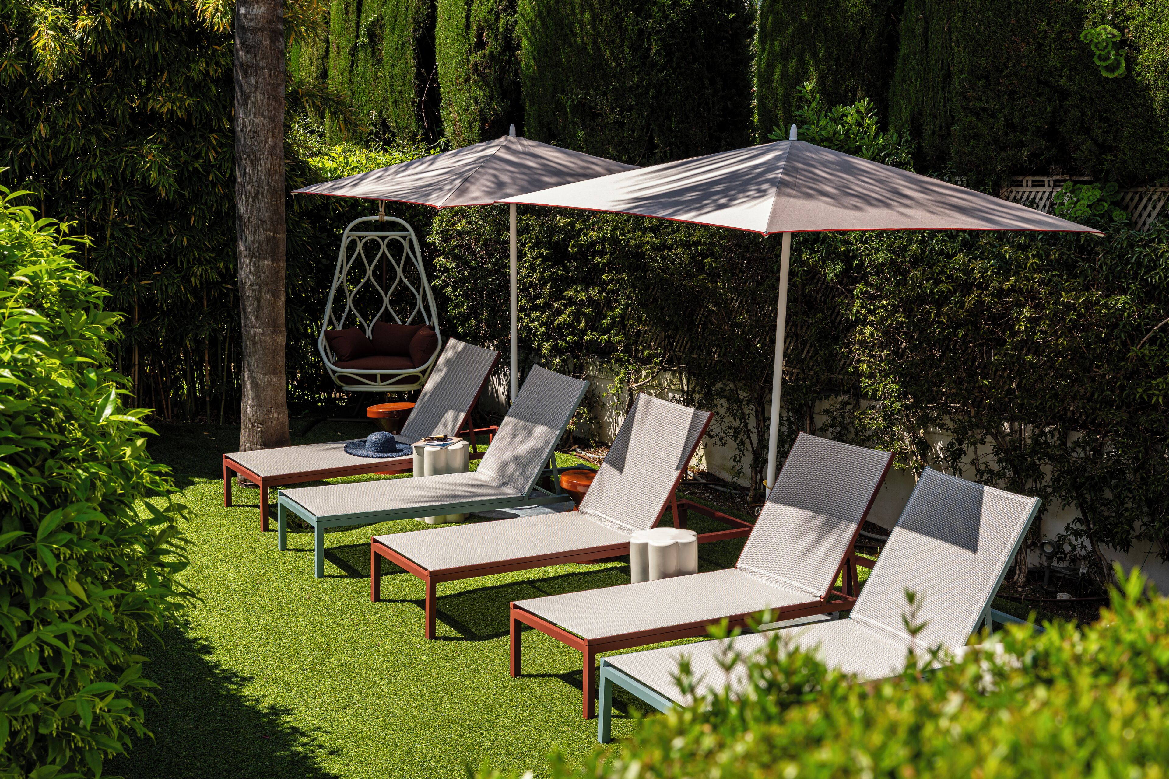 Un jardin agrémenté de quatre chaises longues et de deux parasols, le tout entouré de verdure.