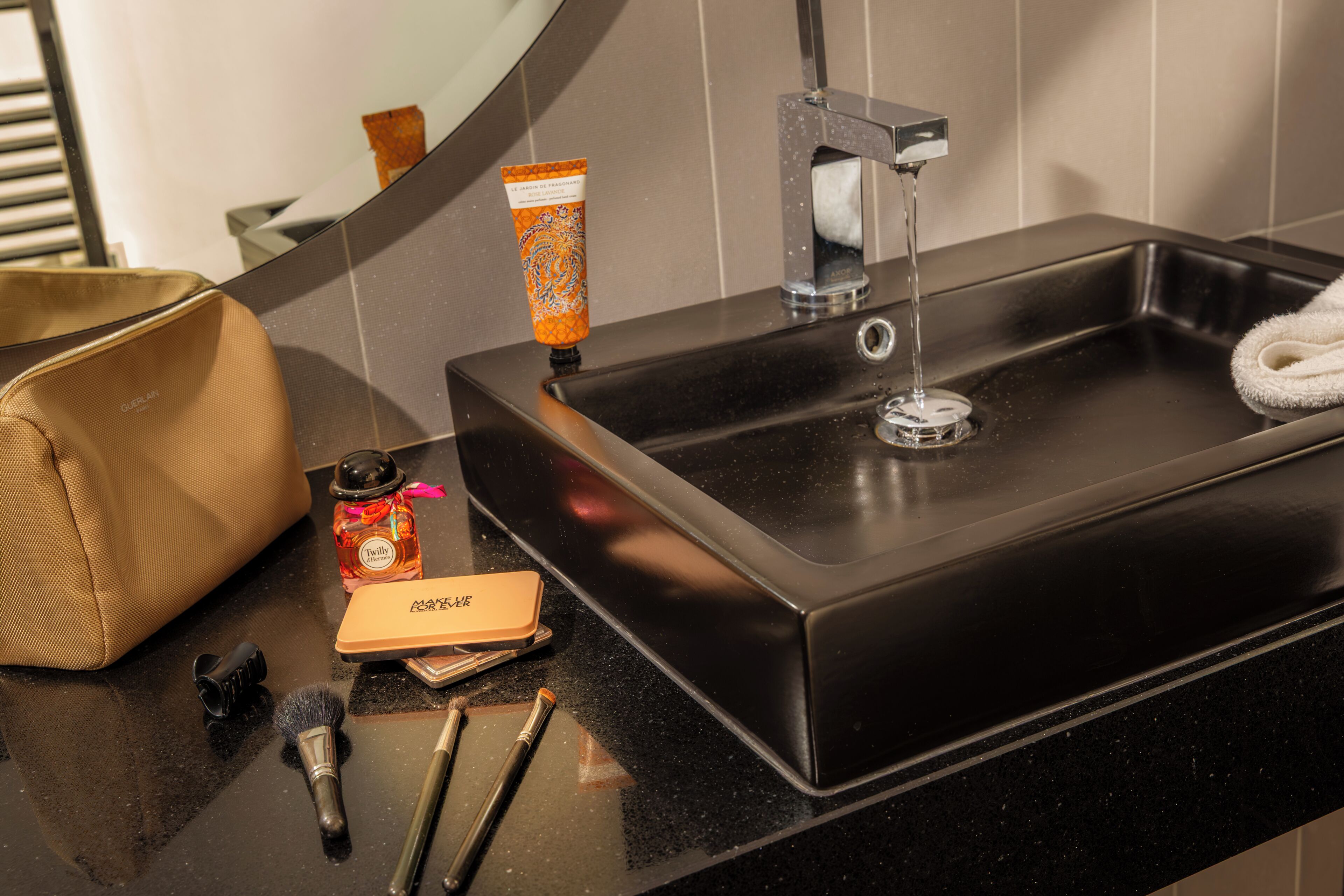 A bathroom sink with a mirror, a towel, a makeup bag, and toiletries.