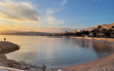 A coastal scene with a calm beach, rocky shoreline, and buildings in the background.