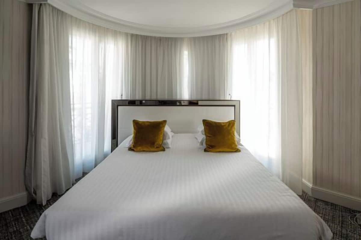 Een hotelkamer met een groot bed, witte gordijnen en een gebogen plafond.