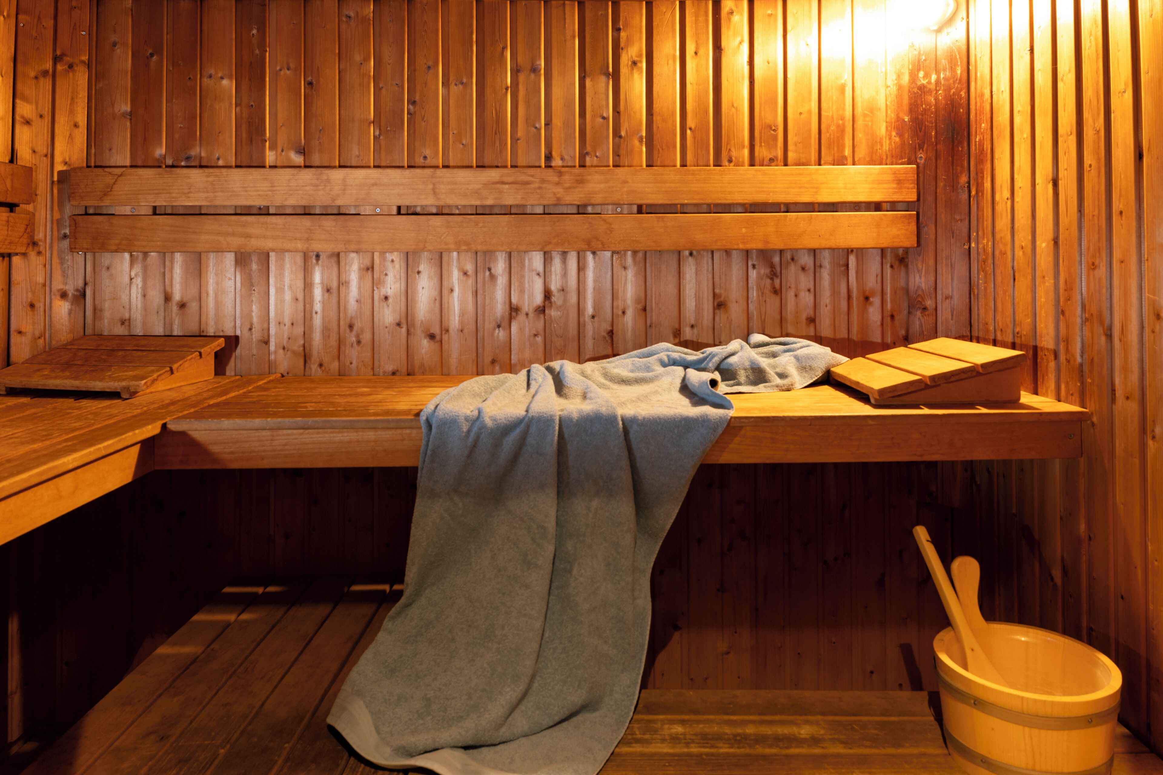 A wooden sauna with benches, a bench with a towel, and a wooden bucket.