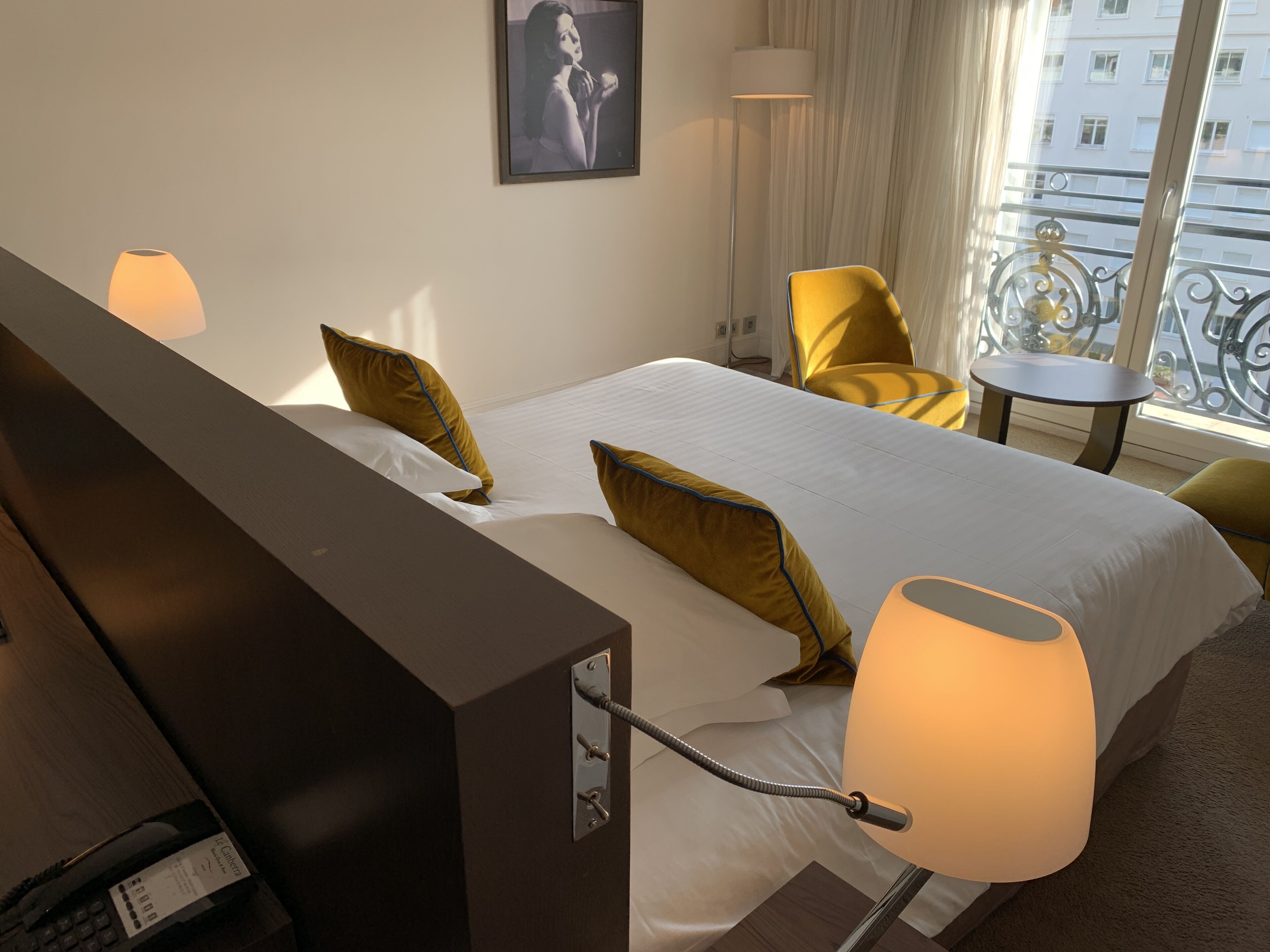 A hotel room with a bed, a desk, a chair, a lamp, and a view of the city through a window.
