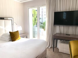 Hotelkamer met een bed, een bureau, een televisie en uitzicht op een gebouw en een cactus.