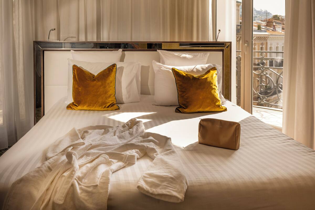 Une chambre d’hôtel avec un grand lit, une fenêtre donnant sur des immeubles et un balcon avec une balustrade.