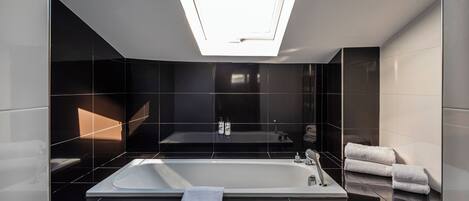 A modern bathroom with a skylight, a large bathtub, and a mirror.