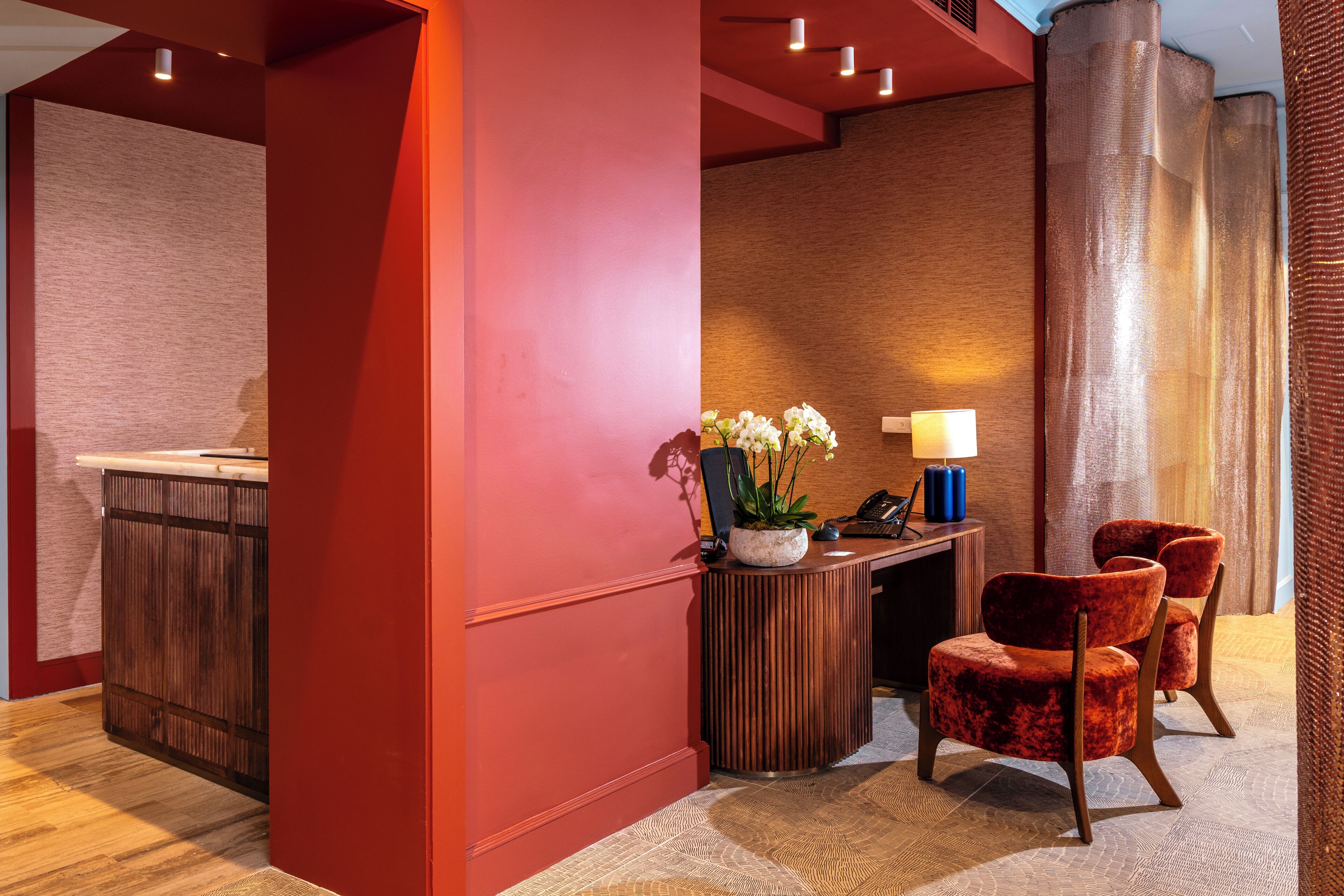 A reception area with a wooden desk, a potted plant, and two red chairs.