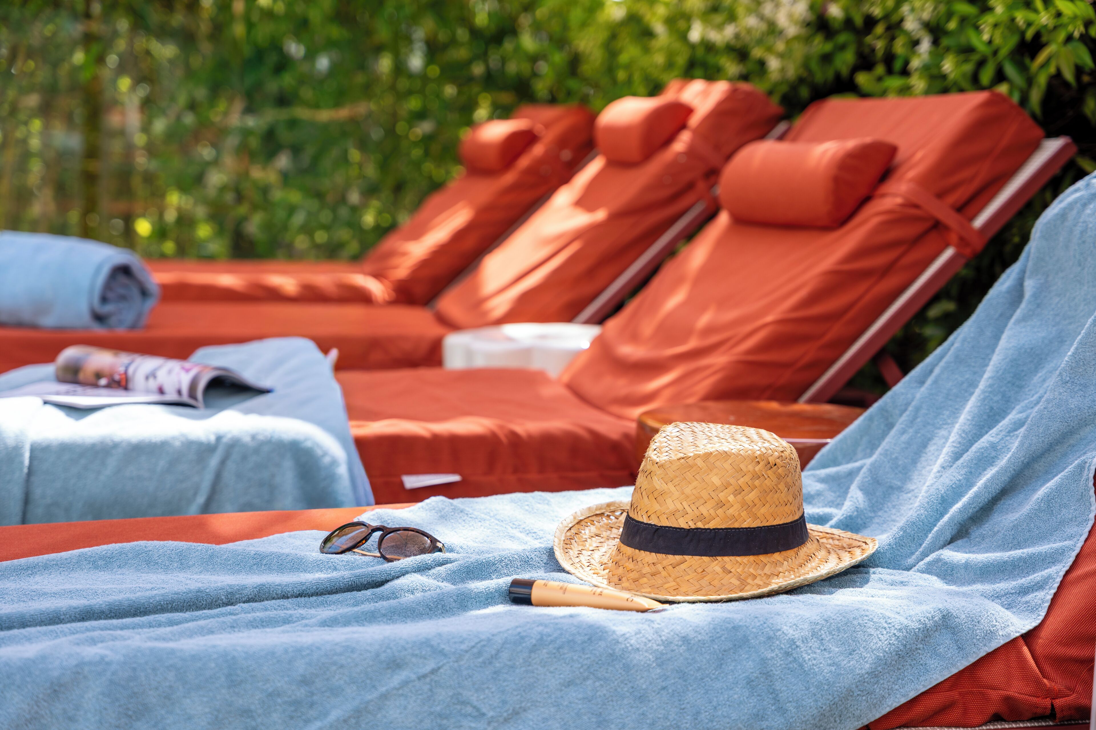 A sunbed with a straw hat and sunglasses, a rolled towel, and a magazine on a blue towel.