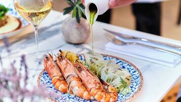 Un plato de camarones a la parrilla con una ensalada y una copa de vino blanco, junto a un jarrón decorativo.