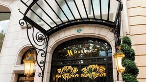 L'ingresso di un hotel con una tettoia ad arco nera, un grande emblema dorato e due lampade fissate al muro.