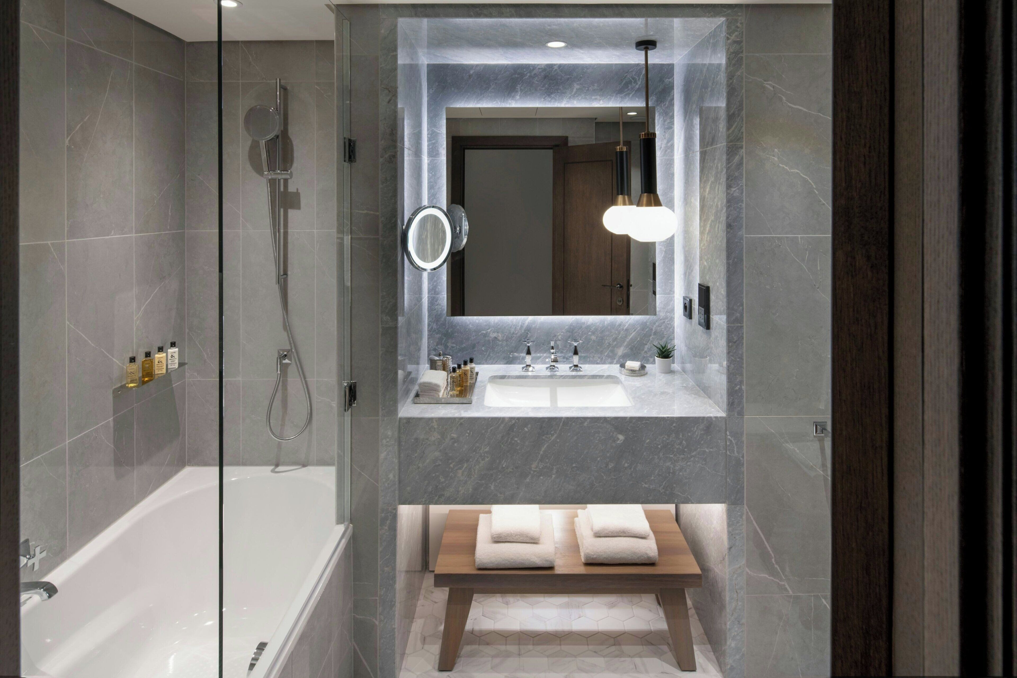A modern bathroom with a glass-enclosed shower, a large mirror, and a wooden bench.
