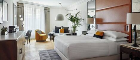 Una habitación de hotel moderna con una cama grande, un escritorio, una silla, una mesita y una planta en maceta.