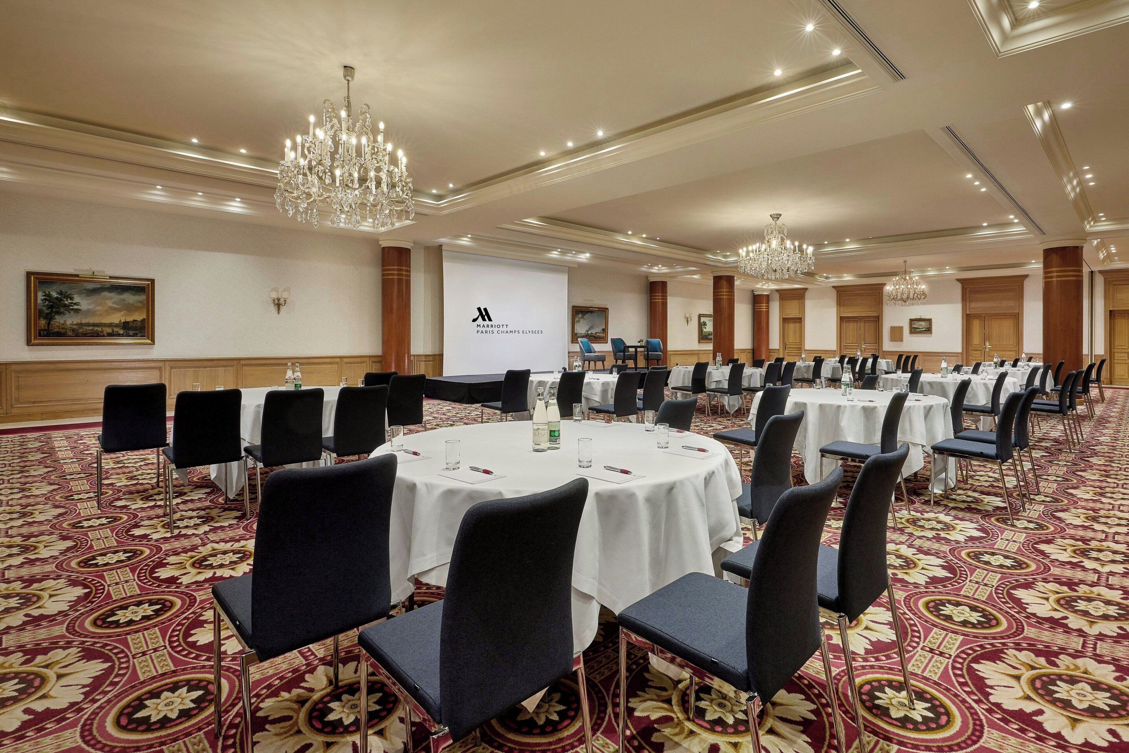 A conference room with round tables, black chairs, and a carpeted floor.