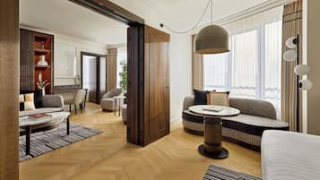A modern hotel room with a sofa, a round table, a coffee table, and a large window with curtains.
