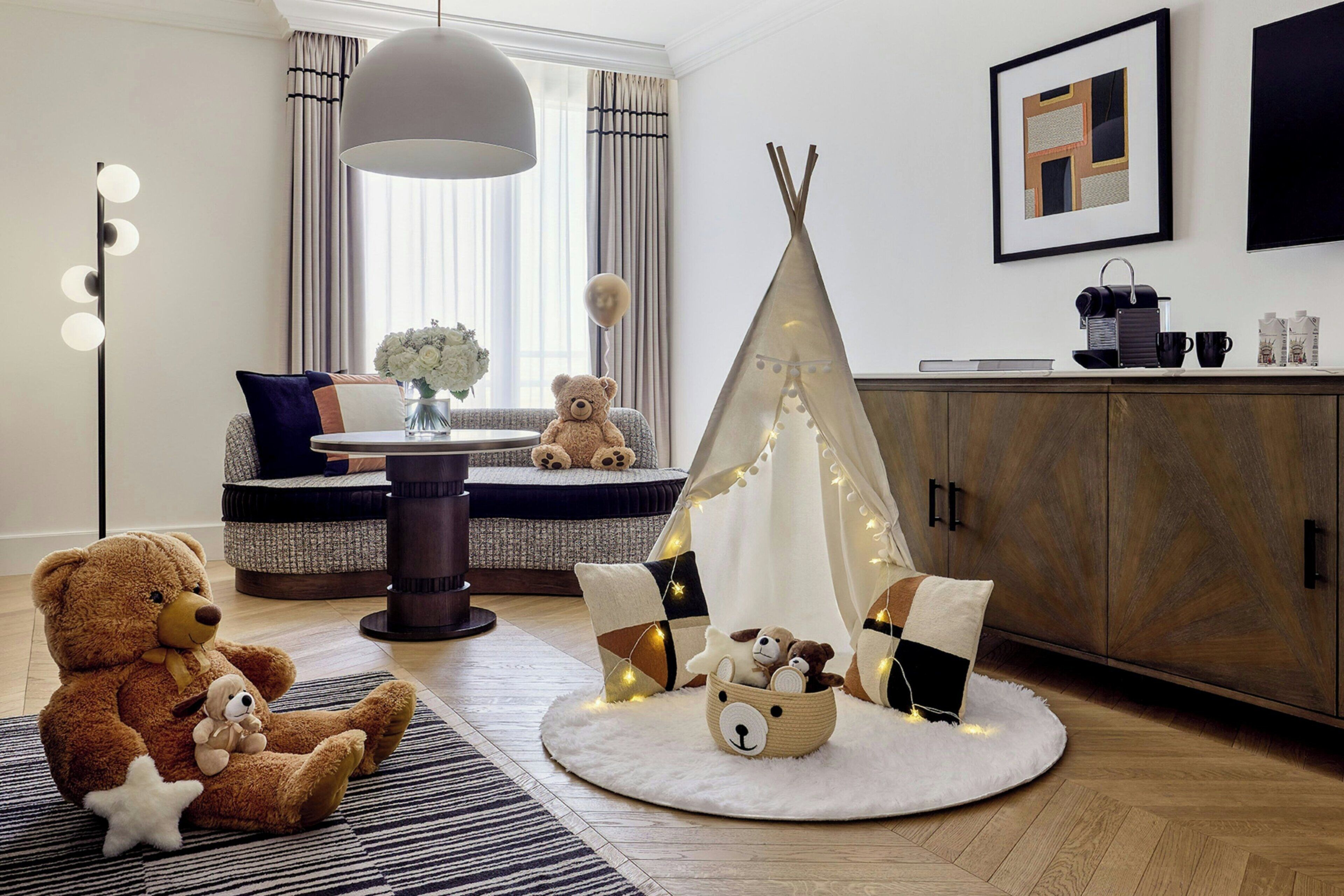 A cozy room with a large teddy bear, a teepee, and a lamp.