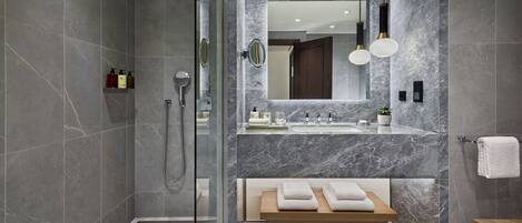 Un baño moderno con ducha envuelta en vidrio, tocador de mármol y banco de madera.