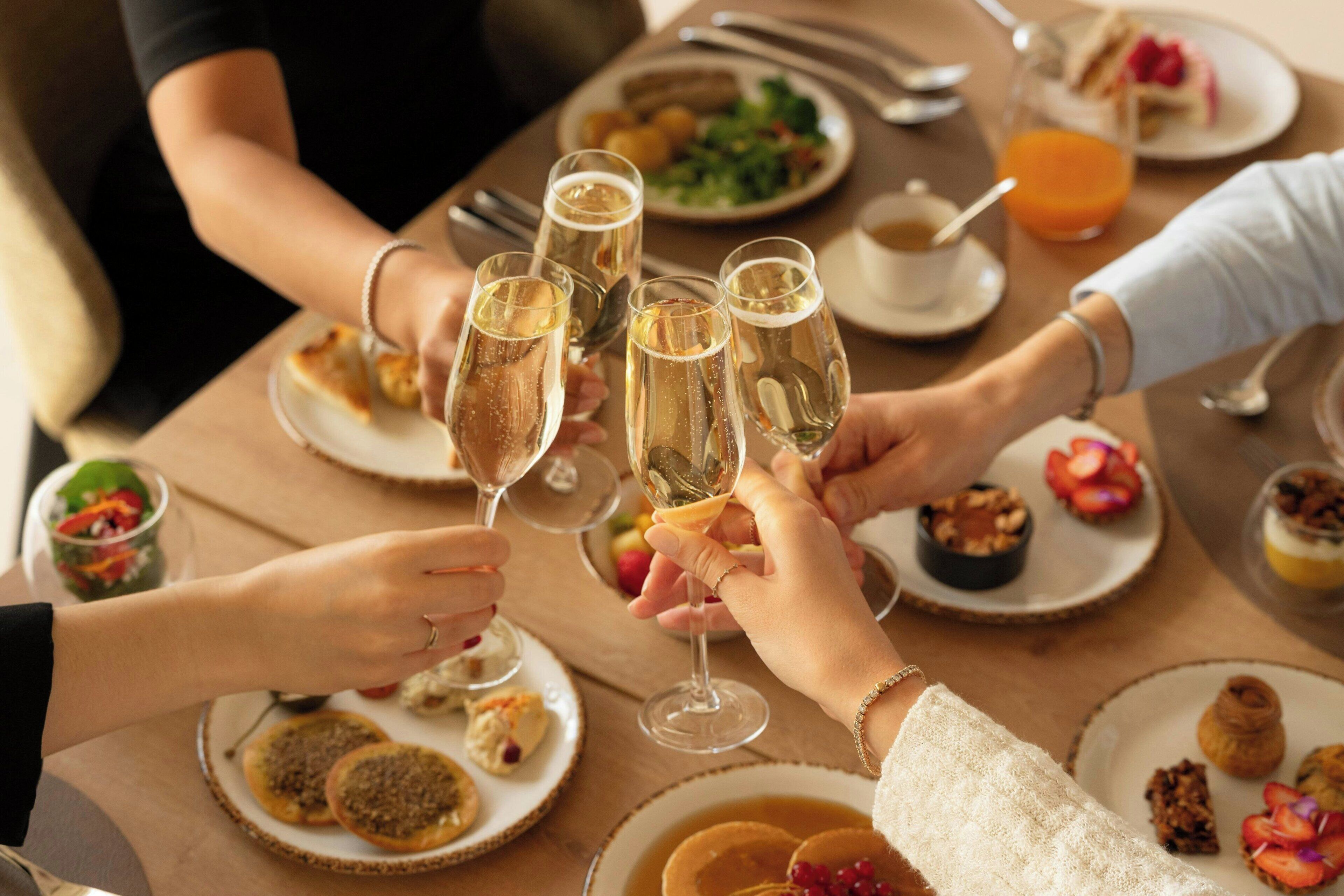 A group of people toasting with champagne glasses at a dining table with various dishes.