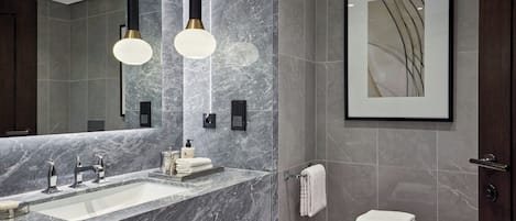 A modern bathroom with a marble sink, two pendant lights, a framed artwork, and a wooden shelf with towels.