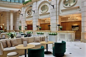 A spacious lobby with a high ceiling, large windows, and a central seating area with a sofa and round tables. - Paris Marriott Champs Elysees Hotel (Paris)